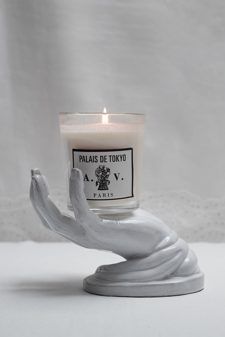 Palais de Tokyo Astier Candle in a hand-shaped holder on a white summerill & bishop broderie anglaise tablecloth background.