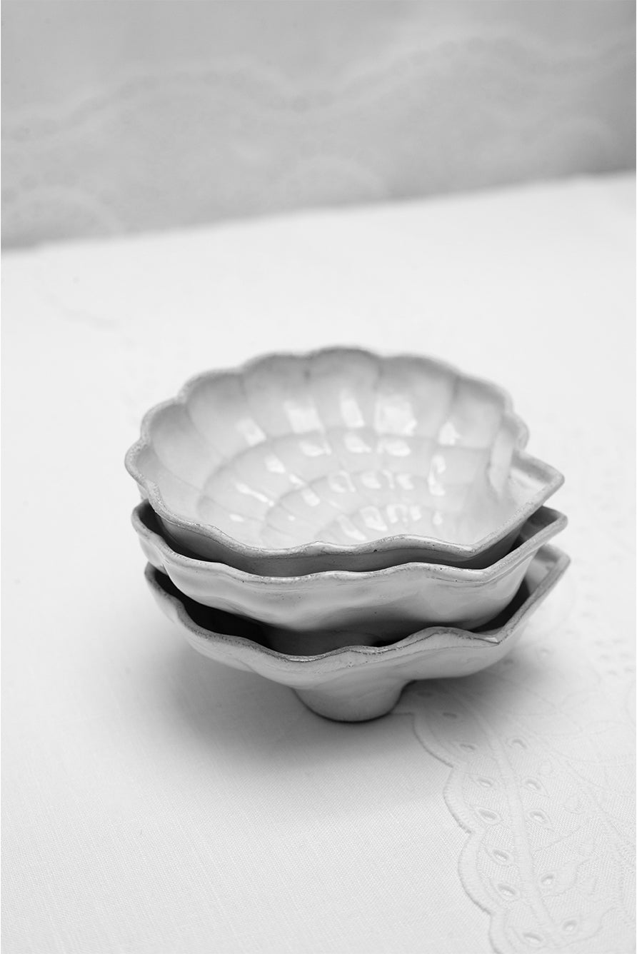 Set of white ceramic shell shaped dishes with scalloped edges on a white broderie anglaise background