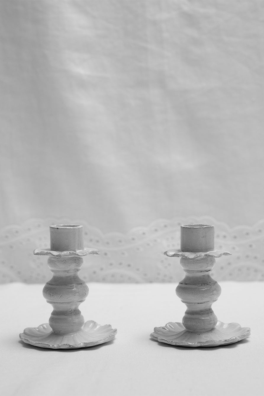 Two white ceramic candle holders on a broderie anglaise linen background