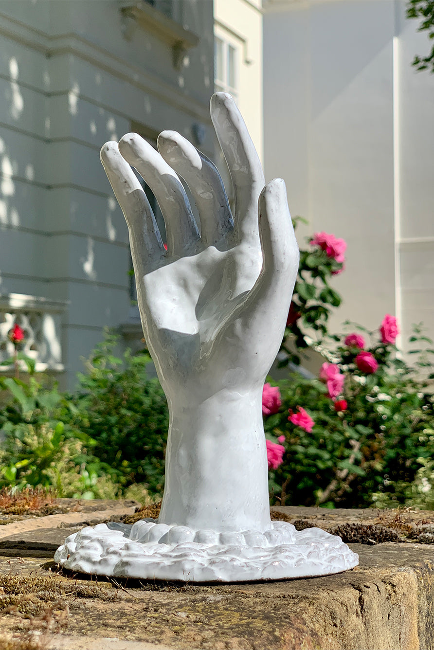 White hand sculpted ceramic on a stone ledge with flowers and building in the background