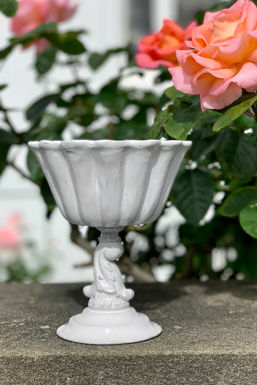 White decorative bowl on stand, on a stone surface with pink roses in the background