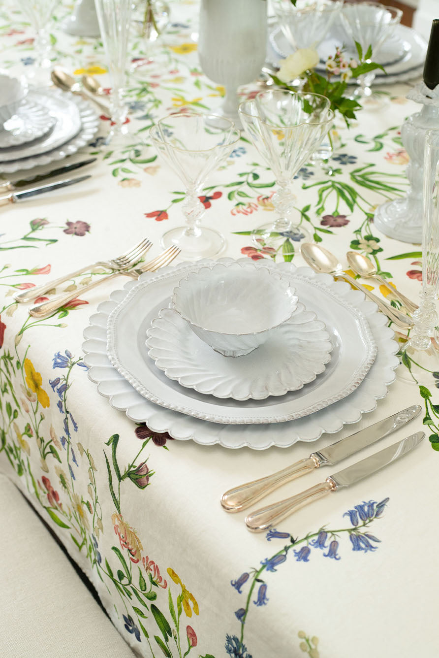 Overhead shot of a dining table setting with floral Botanical Wildflower tablecloth and white ceramic dinnerware by Astier de Villatte.